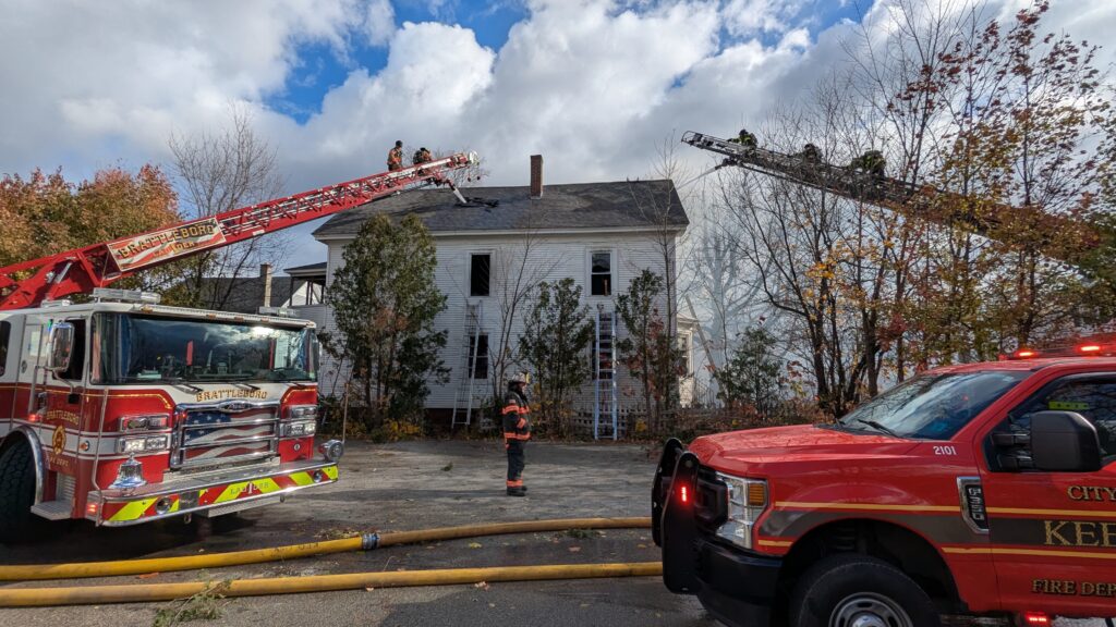 Keene and Brattleboro firefighters spray water through the roof of a building from ladder trucks