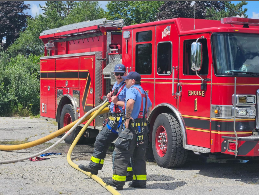 Two KFD firefighters hold hoses in front of fire engine