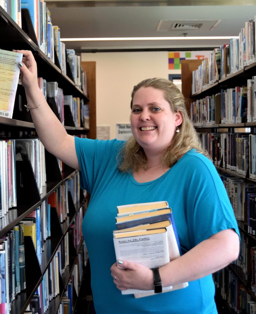 Circulation Manager, Lisa Hoffmann, standing in library stacks to promote Homebound Delivery Services